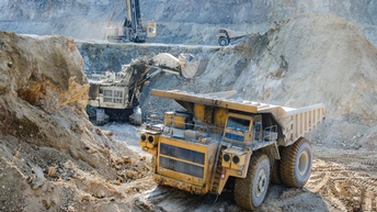 Großer gelber Bautransporter im Fokus in Baugrube stehend, im Hintergrund weitere Baumaschinen wie Bagger und Kräne