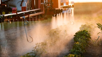 Detailansicht auf Sprühmaschine eines landwirtschaftlichen Gefährts, das Flüssigkeit in Sprühnebel auf Pflänzchen auf Acker sprüht