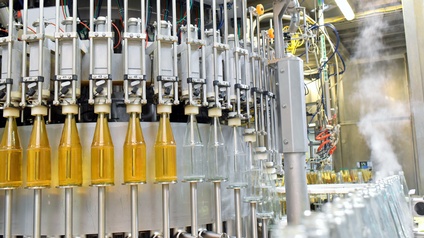 Auf einem Förderband stehen hintereinander in mehreren Reihen viele Glasflaschen. Daneben ist eine Maschine zur Abfüllung der Flaschen. Im linken Bereich sind die Flaschen mit einer Flüssigkeit befüllt, rechts daneben sind sie leer