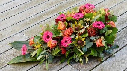 Blumengesteck mit vorwiegend rosa und orangen Blüten auf Holzboden platziert