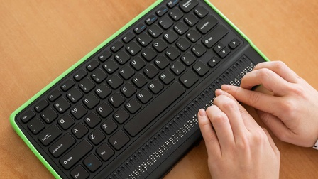 Eine Sehbehinderte Person tippt auf einer Braille-Tastatur